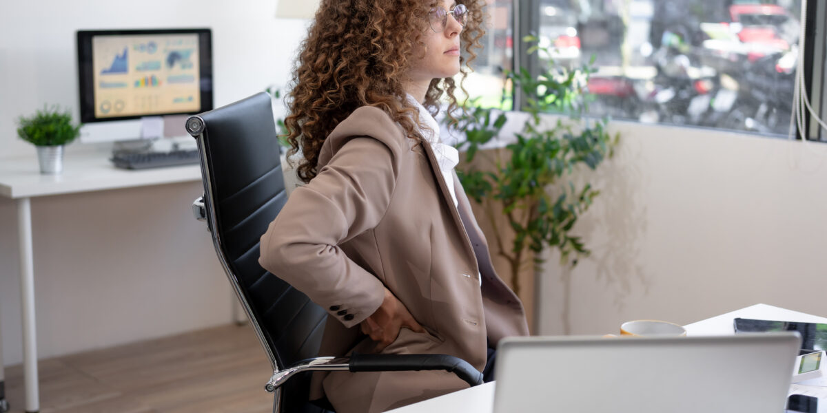 Exhausted professional woman stretching neck while working at office desk with laptop and paperwork, highlighting workplace fatigue, stress management, ergonomics, health awareness, productivity