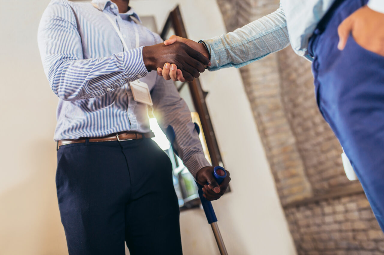 Businessman with a crutch at work shakes hands with his colleague