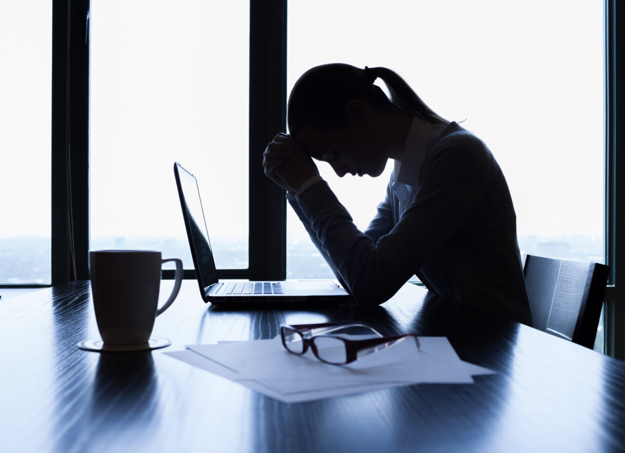 Individual at desk with laptop, reviewing documents and seeking legal advice; office lit by daylight through large windows.