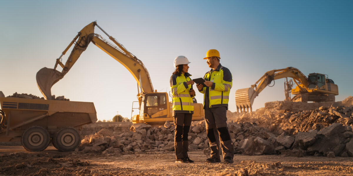 Construction workers confer on a busy site with excavators in use, highlighting workplace injury risks and legal protection needs.