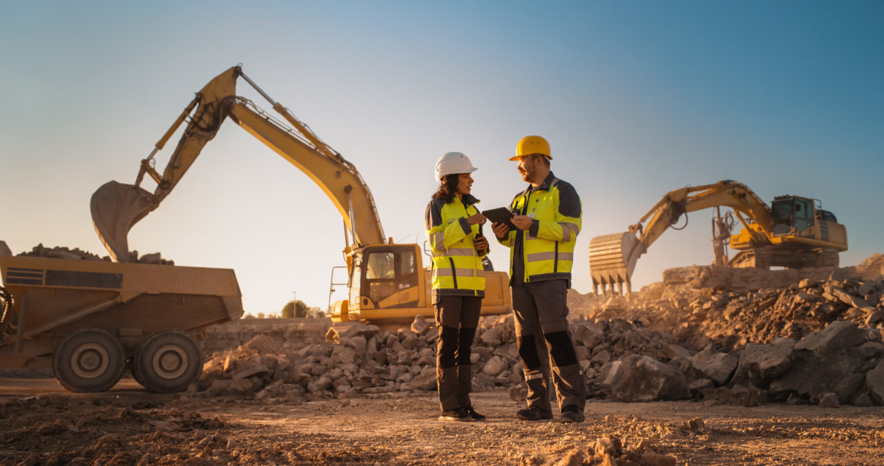 Construction workers confer on a busy site with excavators in use, highlighting workplace injury risks and legal protection needs.